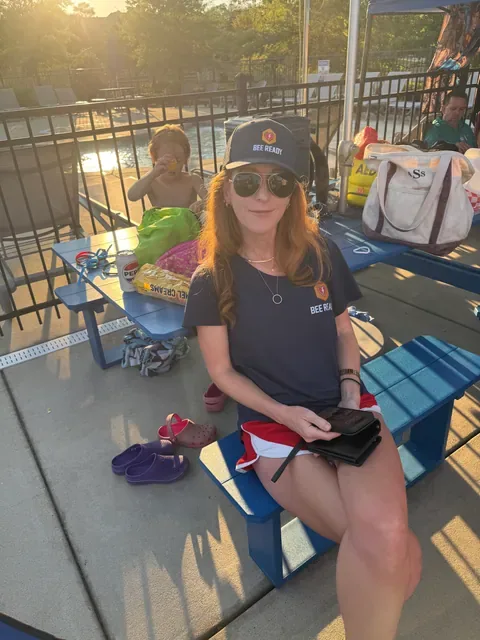 A Bee Ready volunteer sits at a poolside picnic table with a young child and an AED tote bag nearby at the swim meet.