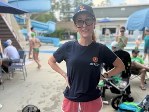 A BeeReady volunteer in a branded hat and shirt standing poolside, ready at the sidelines.