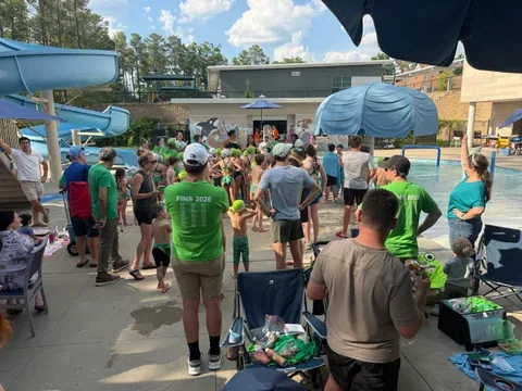 Swimmers and families in green Fins 2026 shirts gathered poolside at the swim meet.