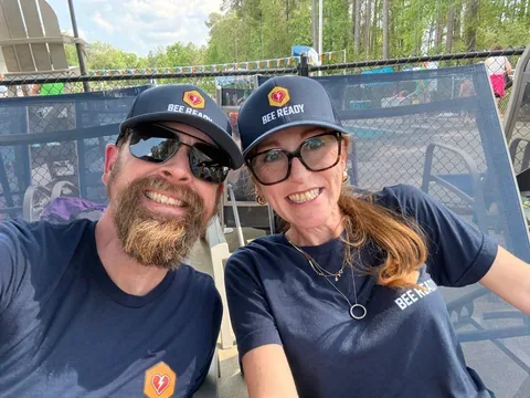 Two BeeReady volunteers in navy hats and shirts smiling for a photo at the swim meet.